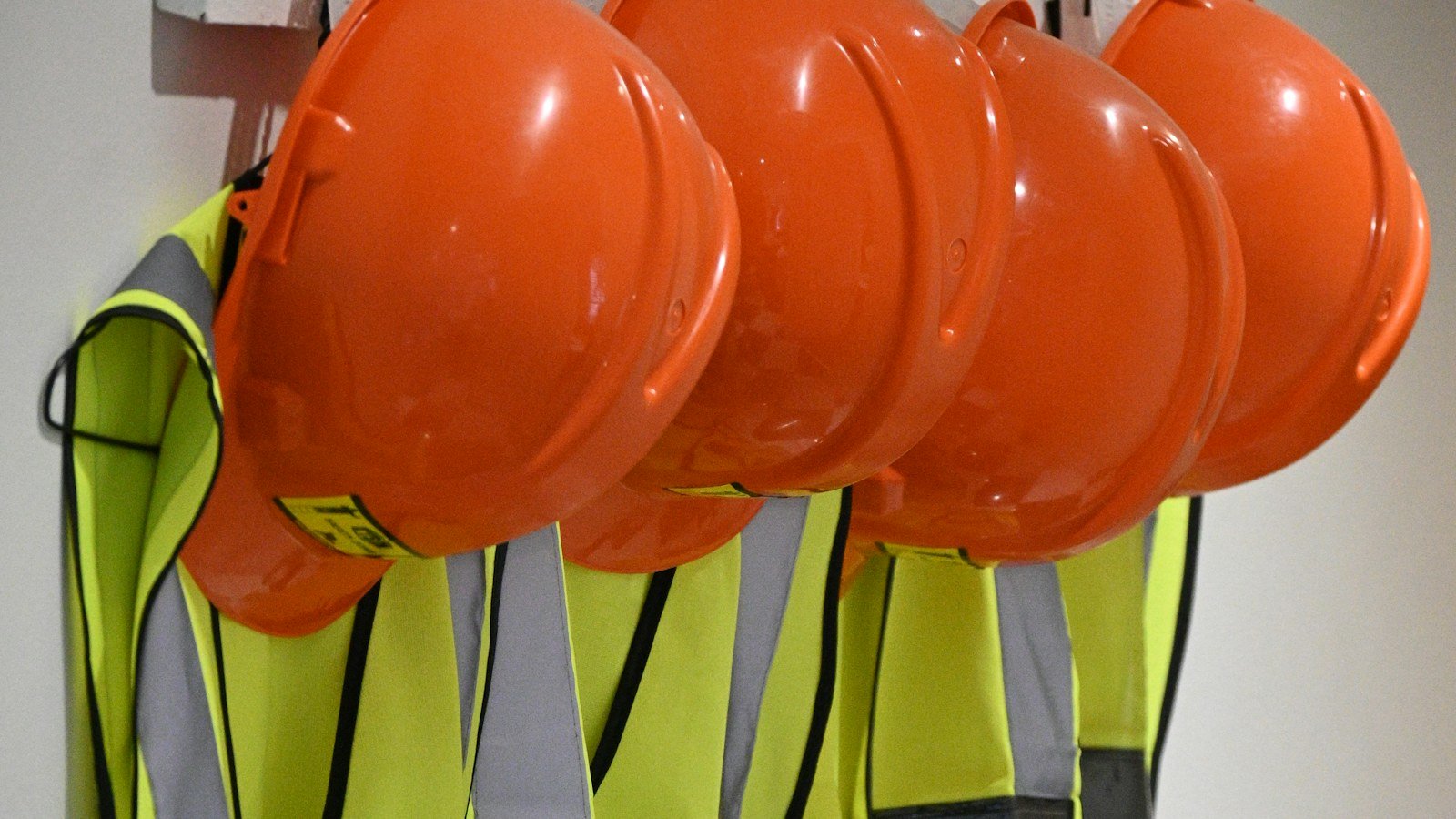 خوذ سلامة وسترات عاكسة معلّقة على الحائط | Hard hats and hi-vis safety vests hanging on a wall