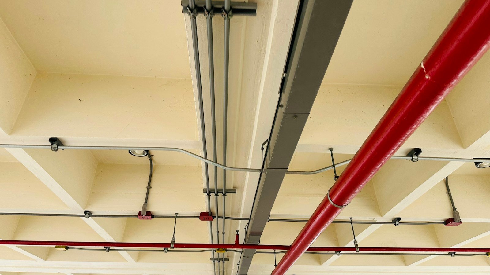 أنبوب رشاشات أحمر ومواسير كهرباء على السقف | Red sprinkler pipe and electrical conduits on a ceiling